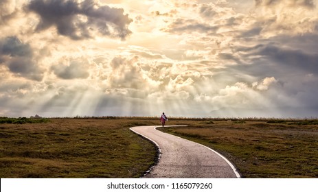 A Person Walking Alone Along S-shape Path. The Sun Produces Amazing Light Rays Across The Sky. The Image Is Simple And Breathtaking. This Image Is Suitable For Background Use Or Add Quote Above.