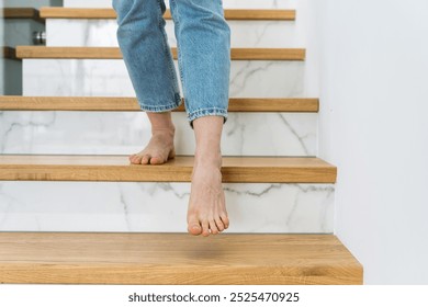 A person walking downstairs at home. Apartment hallway with wooden staircase. Barefoot woman going down the stairs, cropped shot, close up view - Powered by Shutterstock