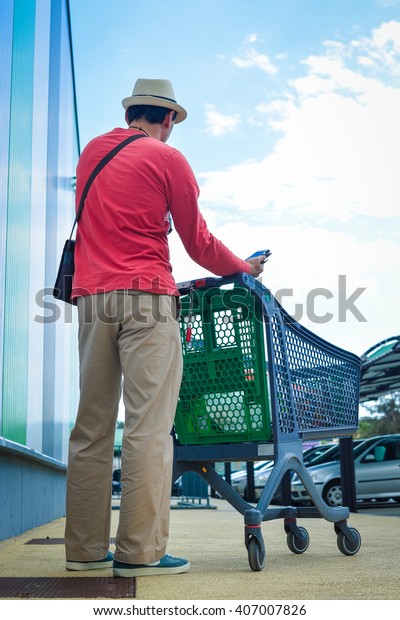 Person walking holding mobile\
smart phone in hand during shopping. Cart on store car park\
background 