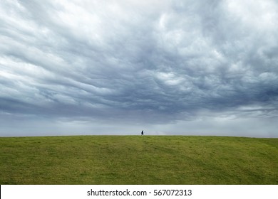 Person Walking On The Horizon With Dark Dramatic Sky Behind. 