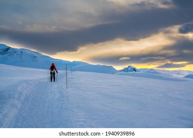 Person Walking On A Mountain Trail In The Snow In A Majestic Artic Wilderness During Sunset.