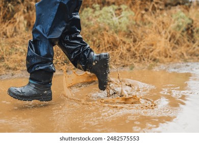 A person is walking through a muddy field with their feet in the water. The scene is wet and muddy, and the person is splashing water as they walk - Powered by Shutterstock