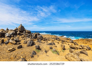 Person walking through rocky landscape along Aruba’s rugged coast, piles of stones stacked on large boulders near the blue Caribbean Sea. - Powered by Shutterstock