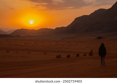 A person walking towards the setting sun in a vast desert landscape, with rocky hills in the background, creating a serene and reflective mood in the open wilderness in Wadi Rum Jordan. - Powered by Shutterstock