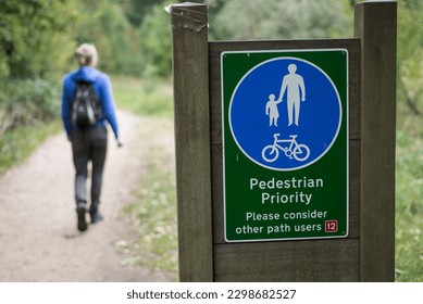 A person walks along a trail in the park passed a sign showing pedestrian priority in London UK