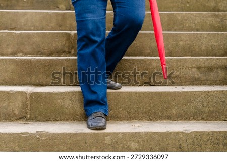 Person walks down steps while holding a red umbrella on a cloudy day in the city