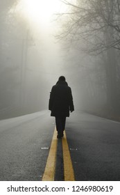 A person walks at the middle of road into to the foggy forest