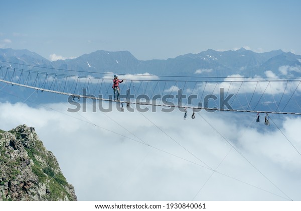 A person walks on\
a suspended rope bridge in the clouds. Extreme attraction.\
Wanderlust and adventures.