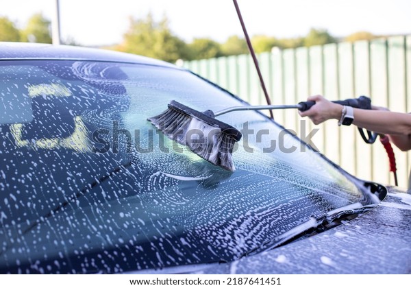 A person washes the window of the car with a\
brush, foam. Selective focus.
