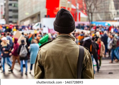 Person watches environmental protest. A young guy wearing a green coat is viewed from behind, watching environmentalists march in the city center of Montreal, Canada