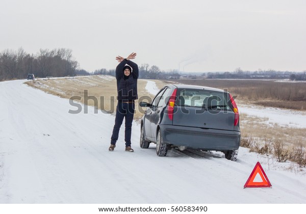 Person waving for help\
with both hands towards an incoming car, he is stuck in rural\
planes waiting for hours, he cannot start his car and engine to\
continue the journey