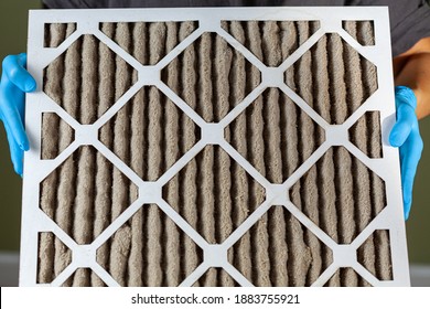 A Person Wearing Blue Gloves Is Holding A Heavily Clogged Dirty Air Filter In Hands Before Replacing It With The New One. Paper Based, Card Board Frame Plated Filters Are Used In Hvac, Ac , Furnaces.