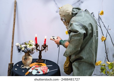 A person wearing a gas mask and a green jumpsuit examines a table with lit candles and a vase of flowers. The table is covered with a black tablecloth. - Powered by Shutterstock