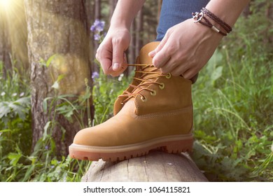 A person wearing leather boots tying sholaces on a fallen tree in the forest. Adventures in the wild.