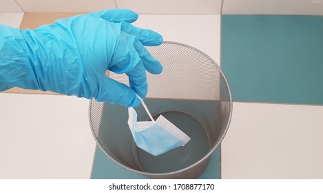 A Person Wearing Nitrile Single Use Glove Throws One Disposable Face Protection Mask Into Trash Can