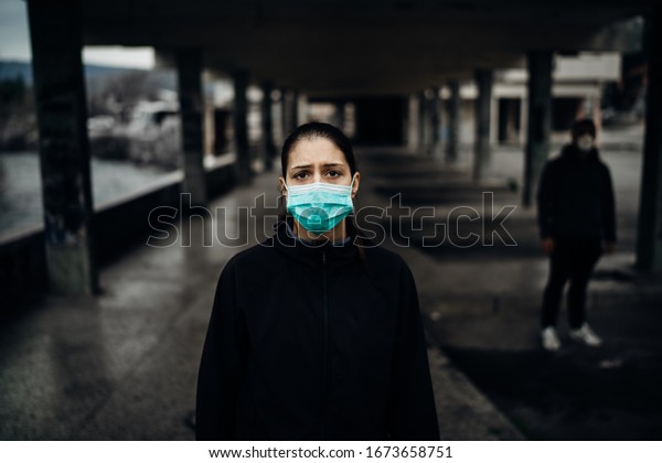 Person\
wearing a protective mask to prevent contagious disease spread.Life\
during epidemic/pandemic.Two people in abandoned place standing\
with distance.Sad woman affected by the\
infection.
