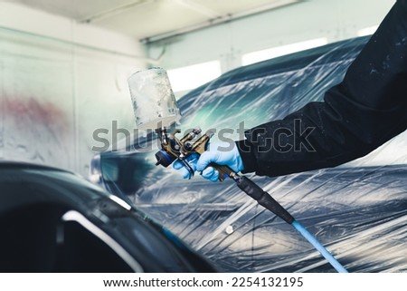 Person wearing protective uniform and blue gloves painting uncovered part of car using airbrush. Car paintwork. Horizontal indoor shot. High quality photo