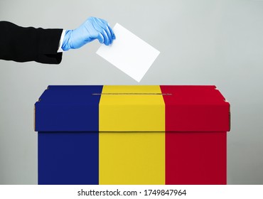 Person wearing suit casting vote in ballot slot,hand in blue PPE protective surgical glove dropping paper in box with ROMANIAN flag,COVID-19 protection & polling station social distancing