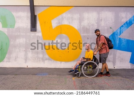 A person in a wheelchair with a cement wall, walking with a friend