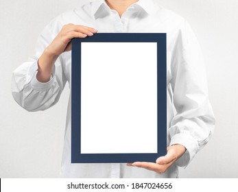 Person In White Coat Holds Empty Mockup Frame. Doctor Holds And Shows The Diploma On Grey Background