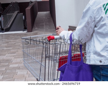 Person in a white jacket pushing an empty shopping cart at the entrance of a supermarket, ready to start grocery shopping
