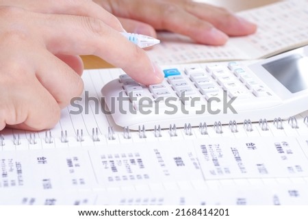 A person who calculates with a calculator while looking at shopping receipts and passbooks written in Japanese