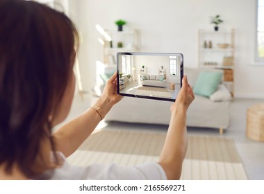 Person who plans on selling house or big spacious studio apartment takes photo on tablet device of clean bright Scandinavian Nordic home interior with stylish sofa, shelves, light walls, large windows