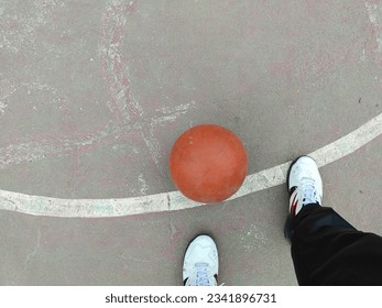 a person who is standing right foot in front and left foot behind wearing white shoes and in front of him there is a basketball ball - Powered by Shutterstock