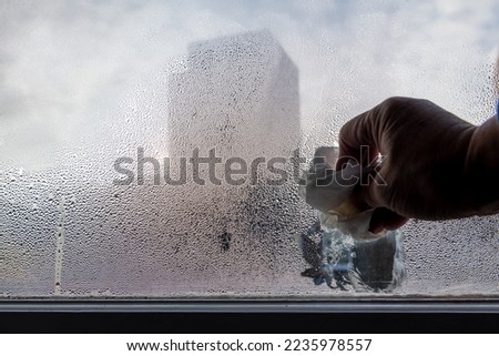 A person wiping condensation of the interior of a window. Winter, cold, heating concept.