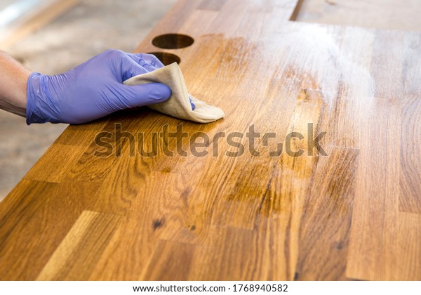 Person working, rubbing oiling with\
linseed oil natural wooden kitchen countertop before using. Solid\
wood butcherblock countertop maintenance\
concept.