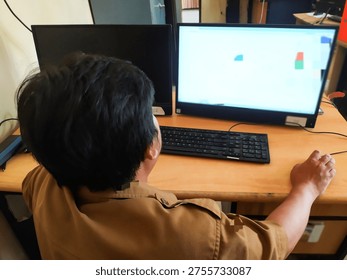 A person working while facing a computer screen in an indoor workspace environment. The scene shows modern work activity, technology use, and daily office routine.