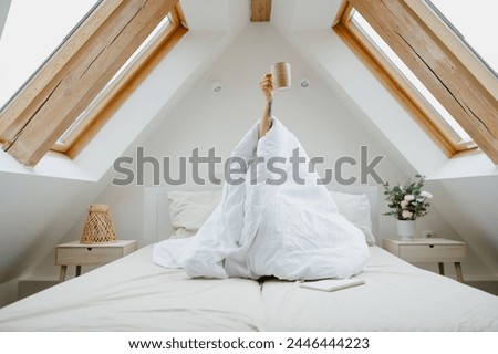 a person wrapped in a blanket is sitting on a bed holding a cup of coffee