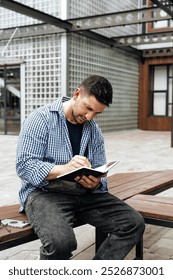 A person writes in a notebook while sitting on a park bench