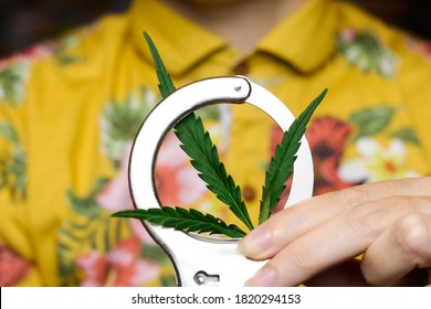 Person In Yellow Fun Shirt In  Handcuffs Holding Hemp Leaf On Handcuff, Closeup. Drug Trade Concept. Selective Focus.