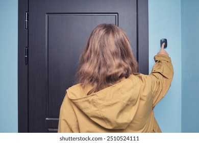 Person in yellow jacket ringing doorbell. Rear view photograph of a person pressing a doorbell button next to a dark wooden door in an indoor setting - Powered by Shutterstock