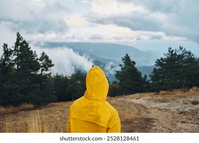 A person in a yellow raincoat standing on a dirt road admiring majestic mountains in the distance - Powered by Shutterstock