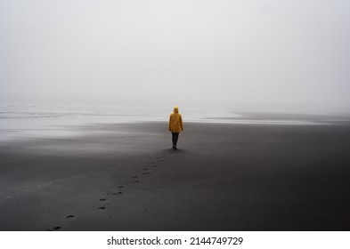 Person In Yellow Raincoat Walking On A Black Beach