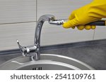 a person in yellow rubber gloves with an adjustable water wrench changes the aerator of the kitchen sink faucet.