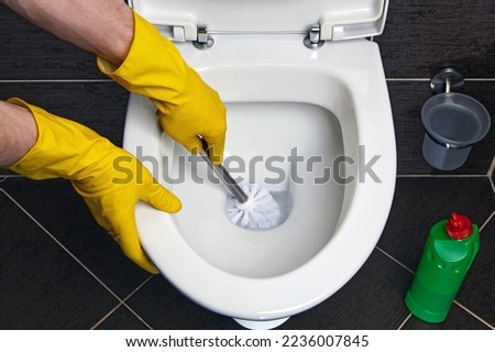A person in yellow rubber gloves cleans the toilet bowl with a brush and disinfectant. Toilet cleaning and disinfection