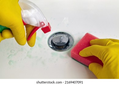 A person in yellow rubber gloves holds a sponge and a cleaning agent for cleaning the washbasin in the bathroom. Housework and plumbing cleaning