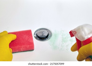 Person in yellow rubber gloves holds a sponge and a cleaning agent for cleaning the washbasin in the bathroom. Housework and plumbing cleaning. Close-up with copy space