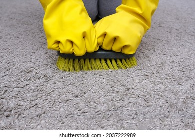 A person in yellow rubber glowes with a brush in hands cleaning carpet in house, cleaning home from dust