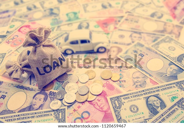 Personal car finance or auto loan concept : Loan\
bags, a white model sedan car, coins on pile of banknotes from\
around the world, depicts the arrangement for installment payment\
or installment loan.