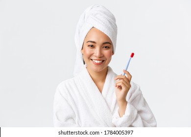 Personal Care, Women Beauty, Bath And Shower Concept. Close-up Of Smiling Attractive Asian Woman Wearing Bathrobe And Towel, Washed Hair, Brushing Teeth With Toothbrush, Standing White Background