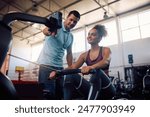 Personal coach assisting sportswoman in using rowing machine during gym workout. Copy space.