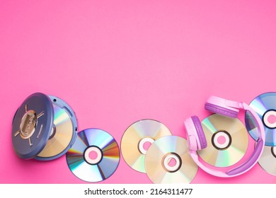 Personal compact portable CD player disks purple headphones on a pink background.