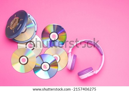 Personal compact portable CD player disks purple headphones on a pink background.