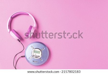 Personal compact portable CD player disks purple headphones on a pink background.