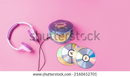 Personal compact portable CD player disks purple headphones on a pink background. Top view layout, copy space, place for text or advertising. Hobby entertainment leisure