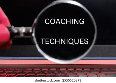 Personal development concept. COACHING TECHNIQUES words through a magnifying glass on a black background.